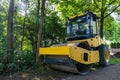 Yellow road roller on the background of forest and lawn. Royalty Free Stock Photo