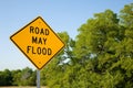 Road May Flood Sign Against A Blue Sky and Green Trees