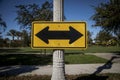 Yellow Road sign on a street pole with arrows pointed in opposite directions facing east and west