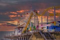 A yellow rollercoaster with flags on top with a colorful Ferris wheel and other colorful carnival games and rides