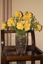 Yellow roses bouquet in glass vase on wooden table with a beige wall and curtain background Royalty Free Stock Photo