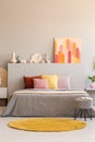 Yellow round rug and stool in front of grey bed with pillows in bedroom interior with poster. Real photo