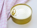 Yellow round tin can near checkered kitchen towel on a white table. Opening a food can with pull tab