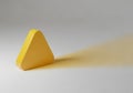 Yellow, rounded triangular prism on a smooth, light surface. It casts a faint shadow to the right, Royalty Free Stock Photo