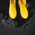 Yellow rubber boots stand in a puddle in which the clouds are reflected.