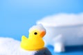 Yellow rubber duck for bathing with foam on a towel on a blue background with a bath, close up Royalty Free Stock Photo