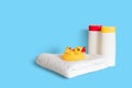 Yellow rubber duck on soft white towel and two plastic white bottles with yellow and red caps on light blue background. Child bath Royalty Free Stock Photo