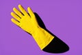 A yellow rubber glove lies on a purple background with strong shadow contrast, creating a bold and minimalistic visual composition Royalty Free Stock Photo