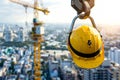 Yellow safety construction helmet on a crane hook, with a panoramic view of the site Royalty Free Stock Photo