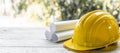 yellow safety helmet and rolled up architectural blueprints on a wooden desk