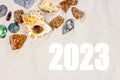 Yellow sandy textured background with bright seashells and stones and 2023 new year numbers top view