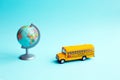 Yellow school bus toy near to globe on blue background Royalty Free Stock Photo