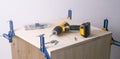 The yellow screwdriver and the cabinet are clamped with clamps. Assembling of cabinet furniture made of wood.