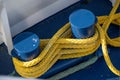 Yellow ship rope tied around blue mooring bollards on a boat deck