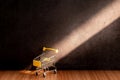 Yellow shopping cart on a wooden table with light and shadow on old gray concrete walls. Royalty Free Stock Photo