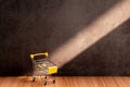 Yellow shopping cart on a wooden table with light and shadow on old gray concrete walls. Royalty Free Stock Photo