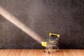 Yellow shopping cart on a wooden table with light and shadow on old gray concrete walls. Royalty Free Stock Photo