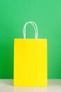 Yellow shopping or gift bag on wooden desk against green background. Royalty Free Stock Photo