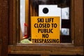 Yellow sign behind wooden window, "SKI LIFT CLOSED TO PUBLIC NO TRESPASSING"