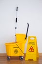 Yellow sign board with mop bucket on floor against wall Royalty Free Stock Photo