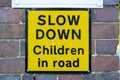 a yellow sign on a brick wall outside a school stating slow down children in road Royalty Free Stock Photo