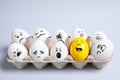 Yellow smiley egg among others with negative emotions in package on light background