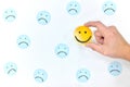 A yellow smiling face icon among a group of sad face emoticons. Positivity, attraction and happiness.