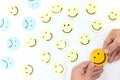 A yellow smiling face icon among a group of sad and happy face emoticons. Positivity, attraction and happiness.