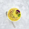 Yellow smoothie bowl with Chia seeds, air wheat and pansy flower on concrete background