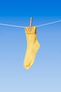 Yellow sock with wooden clothes peg on washing line against blue background Royalty Free Stock Photo