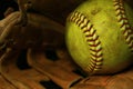 Yellow softball closeup with red seams on a brown leather glove.