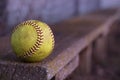 A yellow softball rests on the wooden bench in the dugout.