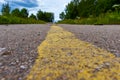 Yellow solid line, grunge road marking on asphalt close up with rural landscape on background