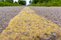 Yellow solid line, grunge road marking on asphalt close up with rural landscape on background