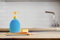 Yellow sponge and bottle with hygiene liquid on wooden table with color cloths, kitchen background, close up Royalty Free Stock Photo