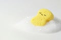 A yellow sponge with a face, lying in foam on a light background. Space for text. Royalty Free Stock Photo