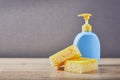 Yellow sponge and plastic clean blue bottle on wooden table with color microfiber cloths, close up Royalty Free Stock Photo