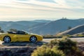 Yellow sports car traveling along a winding road with majestic mountains in the background.