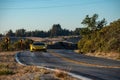 Yellow sports car traveling along a winding road with majestic mountains in the background.