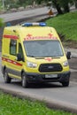 Yellow State Cardiology Ambulance van with siren, blue flashing lights speed driving on city street road to help patient