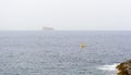 Yellow steel navigational floating buoy - Special Mark - in the blue Mediterranean with a vague Filfla island