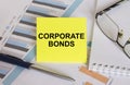 Yellow sticker with text Corporate Bonds lies on financial charts with pen and eyeglass