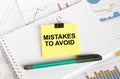 A yellow sticker with text Mistake To Avoid is in a Notepad with a green pen financial charts and documents