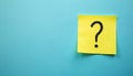 Yellow sticky note with black question mark drawn on blue surface. Represents inquiry doubt uncertainty help needed or problem Royalty Free Stock Photo