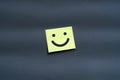 A yellow sticky note with a simple happy smiley face on a dark gray background. Royalty Free Stock Photo