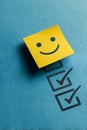 A cheerful yellow sticky note with a smiling face sits above completed checklist boxes on a blue background Royalty Free Stock Photo