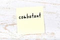 Yellow sticky note on wooden wall with handwritten word combatant