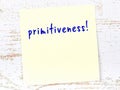 Yellow sticky note on wooden wall with handwritten word primitiveness