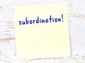 Yellow sticky note on wooden wall with handwritten word subordination