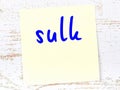 Yellow sticky note on wooden wall with handwritten word sulk